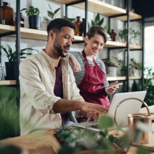 Man and woman shop assistants with laptop working in indoor potted plant store, small business